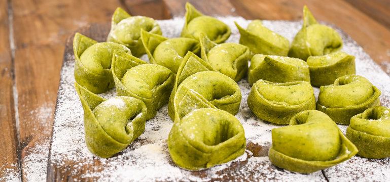 Tortellini e tortelloni typical dishes emilia italy. Food background with homemade raw Italian tortelloni and ingredients for green pesto on wooden background . High angle view. Copy space.