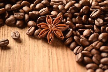Anise and a lot of coffee beans lie on a wooden brown table. There is an empty space at the bottom left.