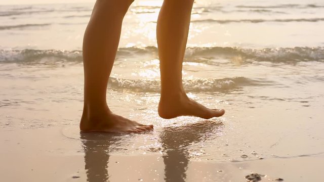 Person walking on the beach at sunset during summer vacation holidays slow-motion, closeup of legs and feet in the sea water, dolly video