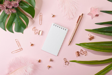 Flat lay of blank notepad, golden office supplies and palm leaves on pink background