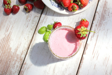Strawberry milkshake or smoothie on white wooden table with fresh strawberries at the background. Top view.