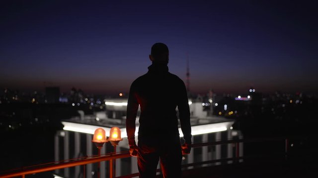 Decisive man looking at night city from roof, escaping in darkness, secret agent