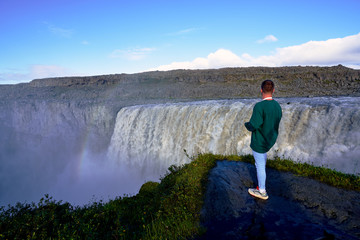 man looking at Dettifoss Waterfall with a beautiful rainbow, the waterfall with the most water in europe and iceland