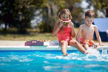 Children have fun in the pool and eating watermelon.