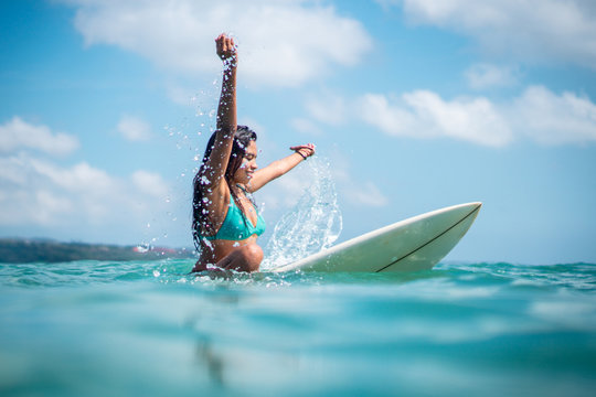 Portrait of surfer girl on white surf board in blue ocean pictured from the water i