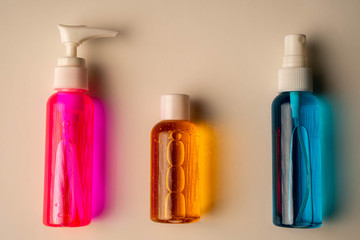 Flat lay of few hand sanitizers arranged on white surface. Top view of tree colorful alcohol sanitizers on cream background