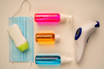 Top view of alcohol sanitizers with face mask and thermometer. Protective mask on cream surface with infrared thermometer, hand sanitizers and disinfectants.