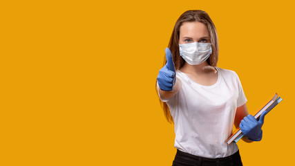 School reopen. New normal. Confident female teacher in protective face mask gloves showing thumb up isolated on bright yellow copy space. Approving sign. Quarantine class. Coronavirus pandemic.