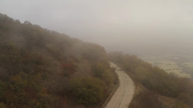 Flight over an old cracked asphalt road into the mountain Aida around Mineralni Bani in Bulgaria on a foggy day.