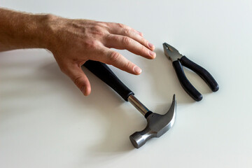 Photo of a hands with hammer and pliers on a white background. Hand tools on beige background. Shot of a hand tools above white wooden table. Used tools on the table. DIY concept with home repairs.