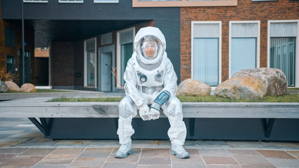 Smiling Man in Spacesuit is Sitting on Wooden Bench. Happy Astronaut Looks at the Camera. Spaceman...