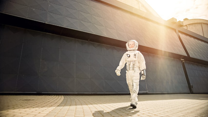 Low Angle Shot of a Confident Handsome Astronaut is Walking Towards Camera from an Industrial Metal Wall. Warm Sun Flare Filter. Man in Futuristic Suit with Technological Panel on His Hand.