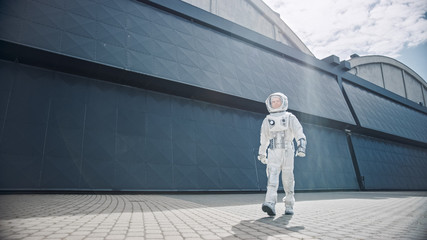 Low Angle Shot of a Confident Handsome Astronaut is Walking Towards the Camera from an Industrial Metal Wall. Man in Futuristic Suit with Technological Panel on His Hand. © Gorodenkoff