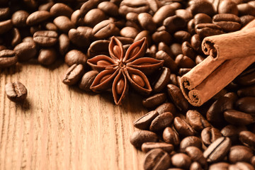 Anise, cinnamon and a lot of coffee beans lie on a wooden table. There is an empty space at the bottom left.