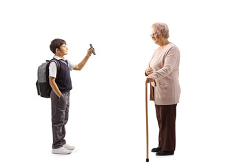 Schoolboy in a uniform standing and showing a smartphone to an old lady with a walking cane