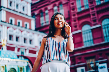 Cheerful asian girl making banking during phone conversation with service operator strolling in downtown, happy young woman having mobile conversation using connection in roaming being on trip abroad