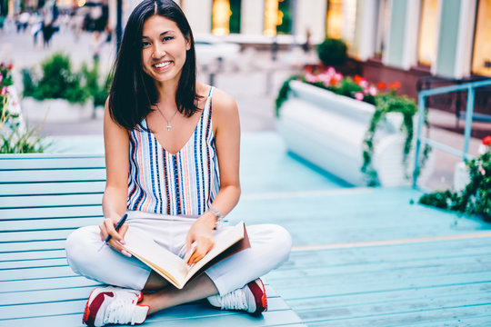 Portrait Of Cheerful Young Woman Sitting With Notebook For Writing Journey Plans Recreating Outdoors, Smiling Female Student Looking At Camera Creating Idea For Graphic Drawings In Sketchbook