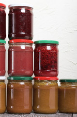 Jam in glass jars. It stands in the form of a pyramid against the background of a light wall.