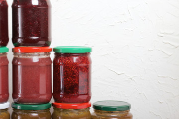 Jam in glass jars. It stands in the form of a pyramid against the background of a light wall.