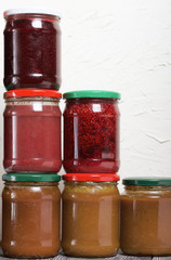 Jam in glass jars. It stands in the form of a pyramid against the background of a light wall.