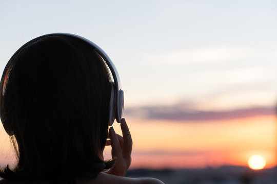 Back View Silhouette Of Relaxed Woman Wearing Headphones Meditating Listening To Music On The Beach At Sunset