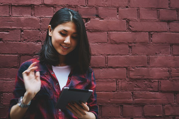 Happy young hipster girl holding modern digital tablet and messaging while enjoying time near copy space area, cheerful female blogger using touch pad installing application and browsing 4g internet