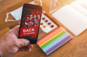 Items for the school, phone with COVID-19 warning and protective mask on dark wooden table. School supplies on dark board background during pandemic COVID-19. Back to school during pandemic.