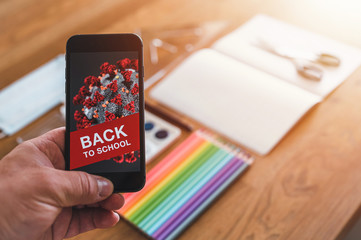 Items for the school, phone with COVID-19 warning and protective mask on dark wooden table. School supplies on dark board background during pandemic COVID-19. Back to school during pandemic.