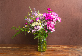Bouquet of field flowers in glass vase on brown table