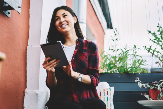 Successful Smiling Blogger Resting Outdoors While Looking Away And Holding Contemporary Touch Pad, Happy Asian Woman 20 Years Old Messaging With Friends Using Digital Portable Pc Ang 4g Internet