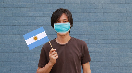 Masked man in brown shirt and small Argentina flag in hand. Concept of protection COVID.