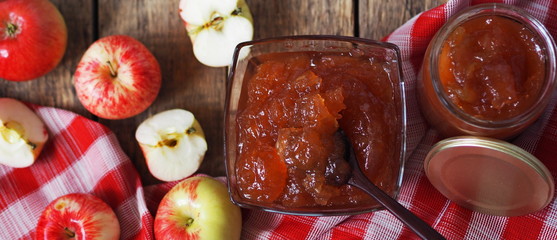 Autumn preparations of homemade apple jam for future use. Jam in a glass vase on the background of a wooden table with apples.