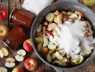 The process of making jam. We boil apple jam and close it in jars for future use.Wooden background with apple jam, apples, glass jars and a saucepan with chopped apples.