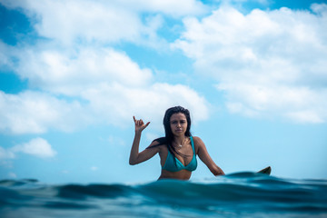 Portrait of surfer girl on white surf board in blue ocean pictured from the water