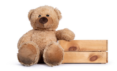 Cute new light brown toy teddy bear sitting facing sitting beside wooden crate. Isolated on white background.