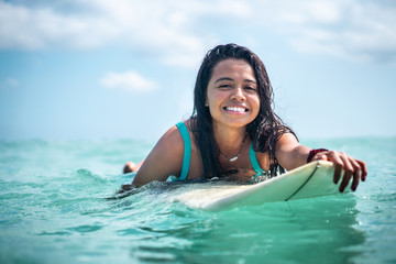 Portrait of surfer girl on white surf board in blue ocean pictured from the water