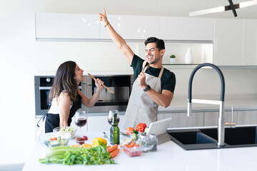 Couple Holding Spatulas And Singing In Kitchen