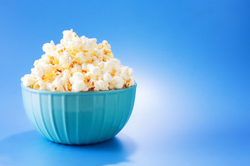 Blue bowl full of fresh popcorn, isolated on blue background, with available copy space.