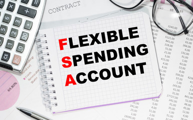 Put a FLEXIBLE SPENDING ACCOUNT on a notepad against the background of graphs and financial statements, next calculator, pen and glasses. Business concept.