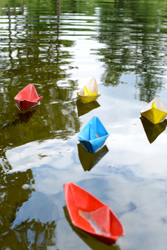 Multicolored paper boats float down the river. Childhood and dream concept