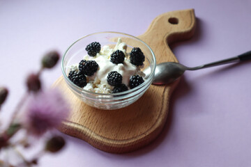 Light Breakfast of cottage cheese and blackberries in a glass Cup on a wooden Board, top view, bokeh