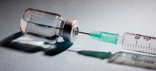 Vaccine vial dose and syringe against gray background