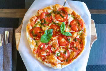 Pizza margarita with tomatoes sauce cheese basil on a wooden tray interior of a fast food cafe
