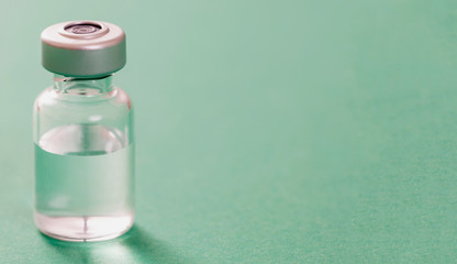 Medical vial for injection on green background, transparent glass bottle, drug medicine vaccine dose.