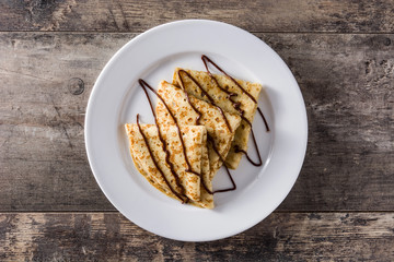 Sweet crepes with chocolate syrup on wooden table