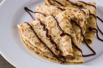 Sweet crepes with chocolate syrup on wooden table.Close up