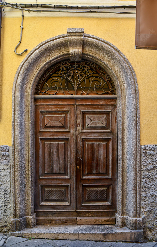 Wall mural close-up of an old wooden door with arched stone frame on a yellow wall, italy