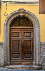 Close-up of an old wooden door with arched stone frame on a yellow wall, Italy