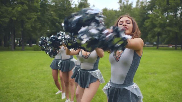 Portrait of beautiful cheerleader girls standing in line and dancing with pompoms outdoors
