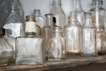 Close up of empty flask on shelf with many dirty old glass bottles. All bottles are clear but have been exposed to the outside. Focus on flask, soft background. Texture Background.